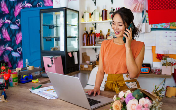 A young female flower shop owner on the phone in front of her computer